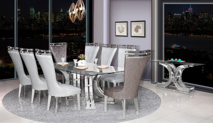 A modern dining set including a glass dining table with a metal base and eight upholstered chairs in white and gray colors, set in a room with large windows.